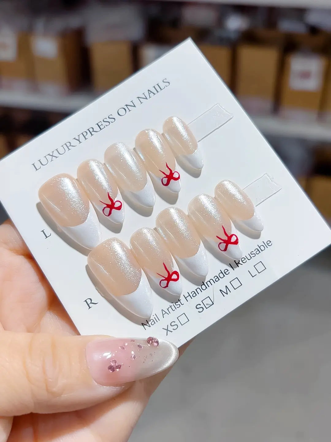 angled view showing nude shimmer base and white tips with red bow, handmade press on nails