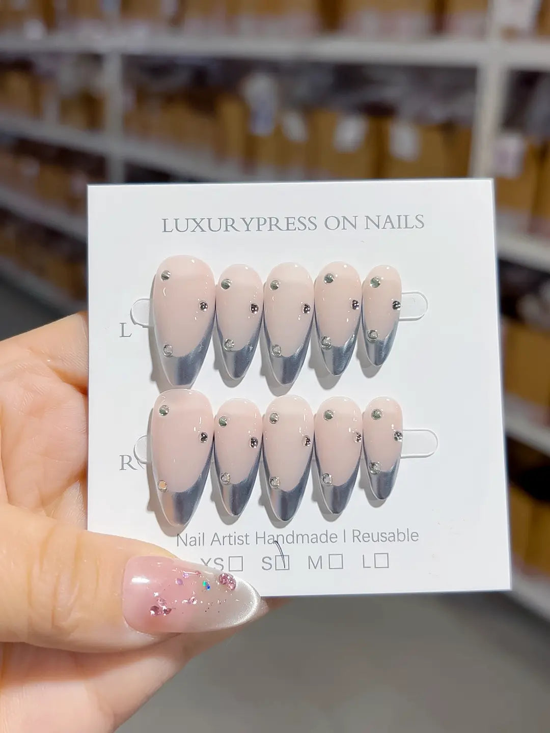 handmade press on nails, medium almond nude base with silver chrome french tips and 3D rhinestones, angled view