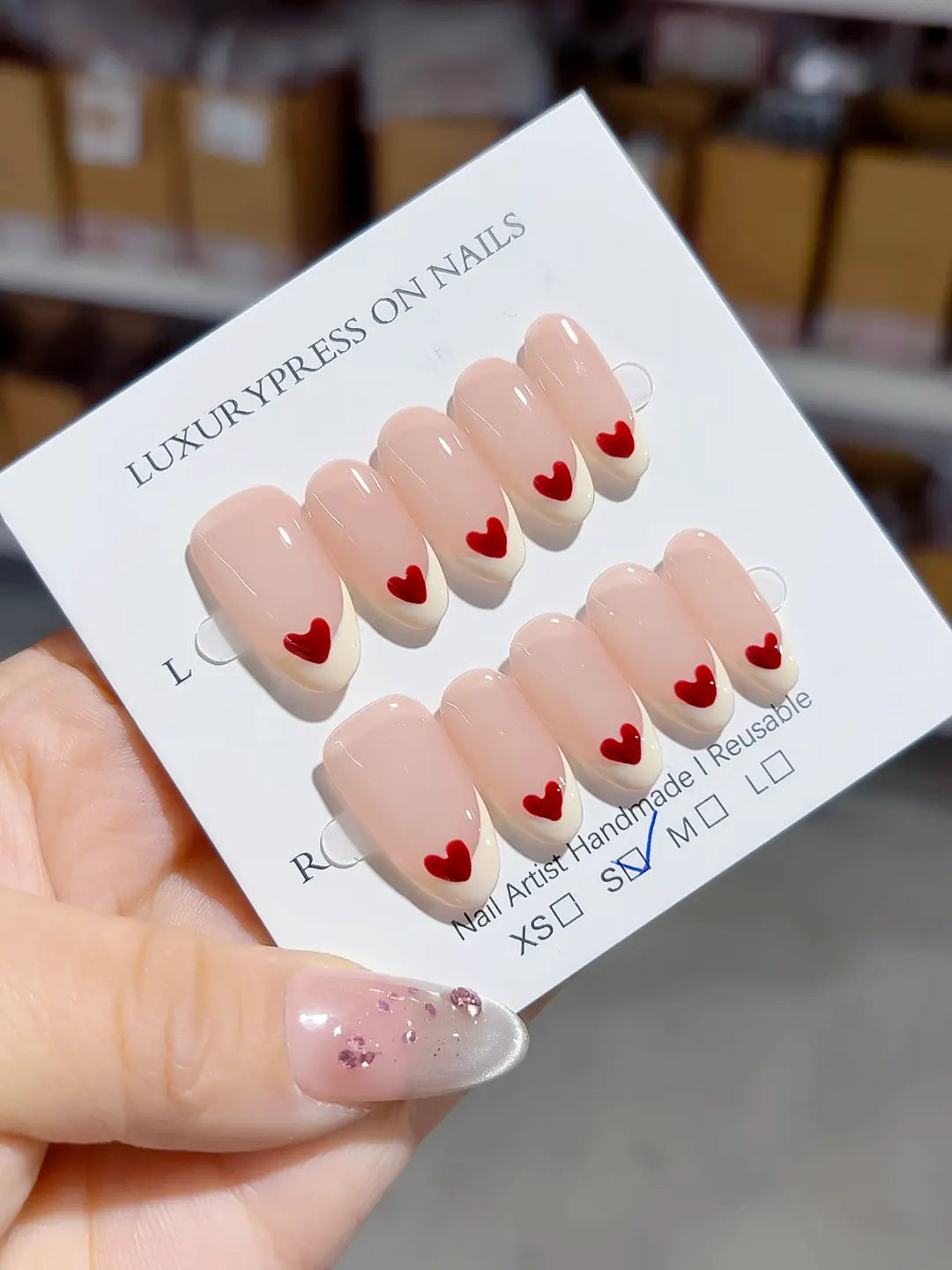 handmade press on nails, medium oval nude french with red heart accent on each tip, angled view