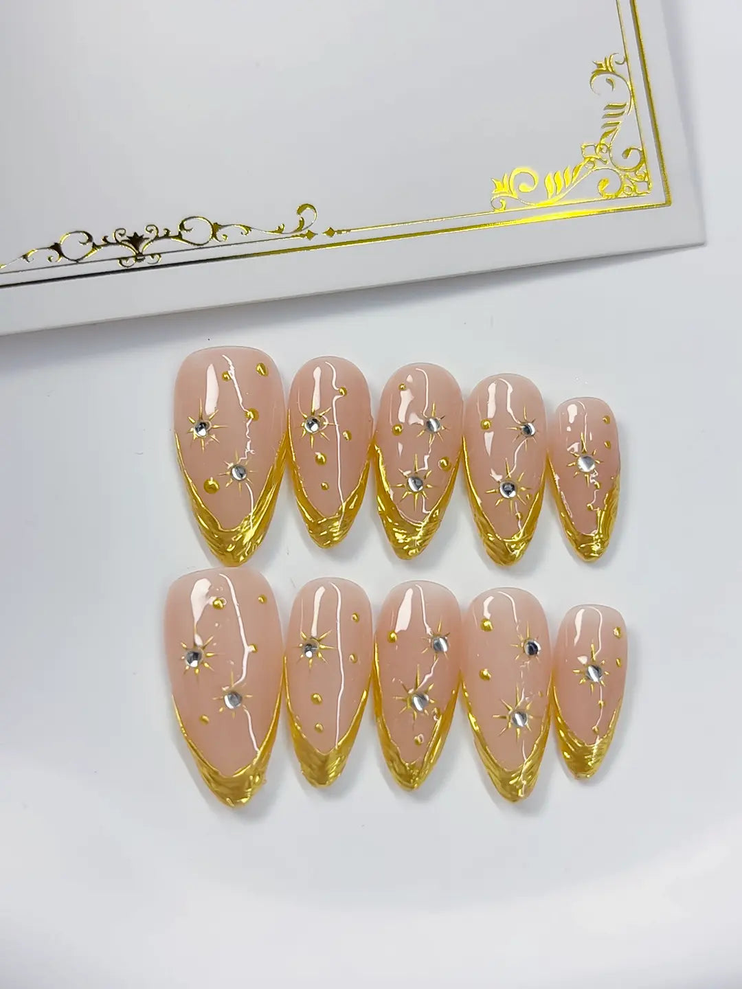 Angled view highlighting metallic gold edges and 3D rhinestones on select nails