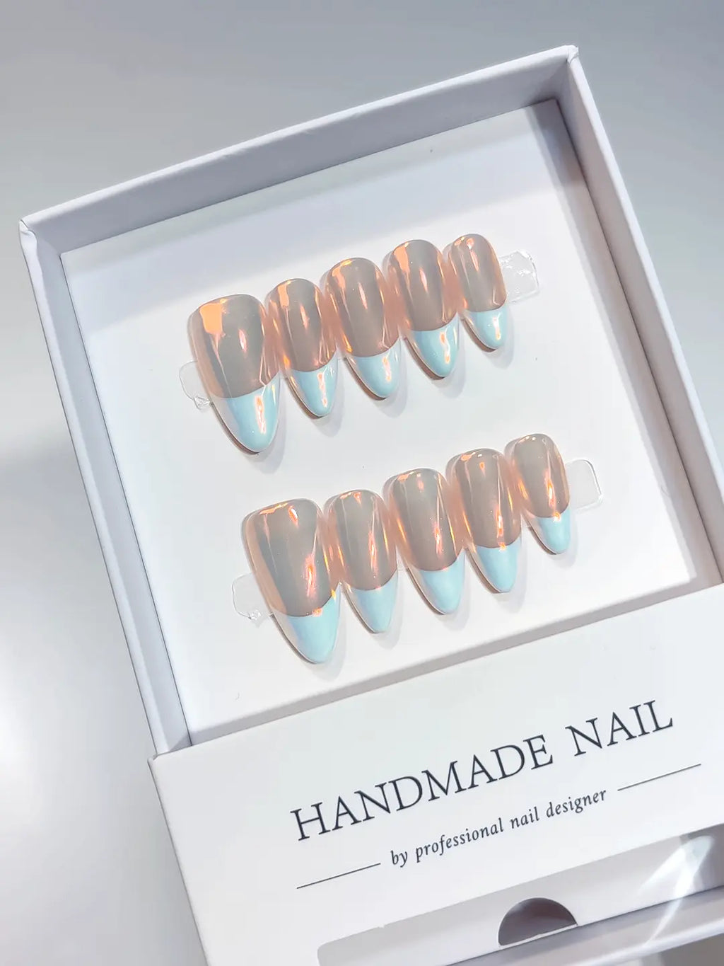 Blue French tips on medium almond handmade press on nails with orange aurora chrome finish in a designer box.
