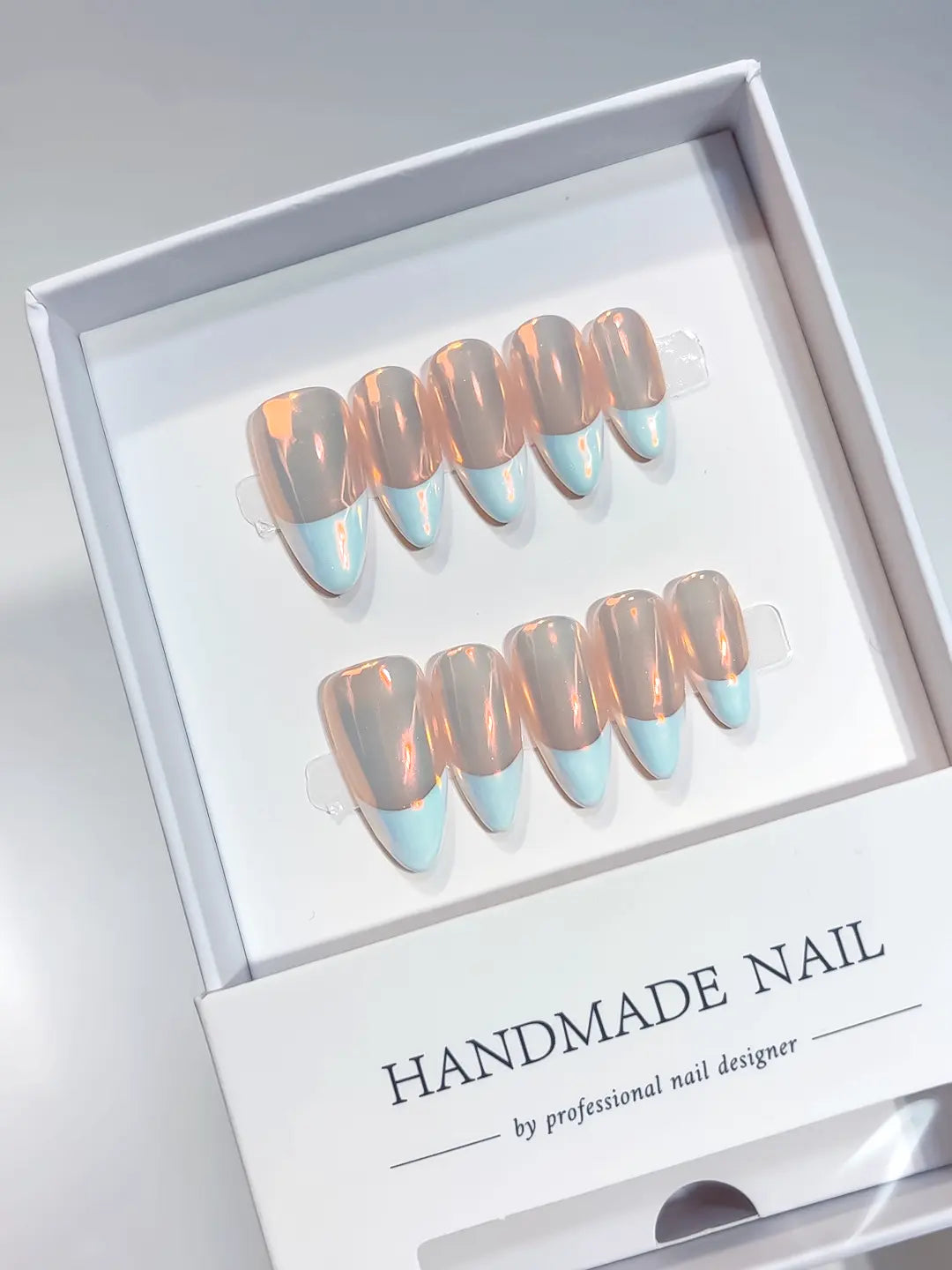 Blue French tips on medium almond handmade press on nails with orange aurora chrome finish in a designer box.
