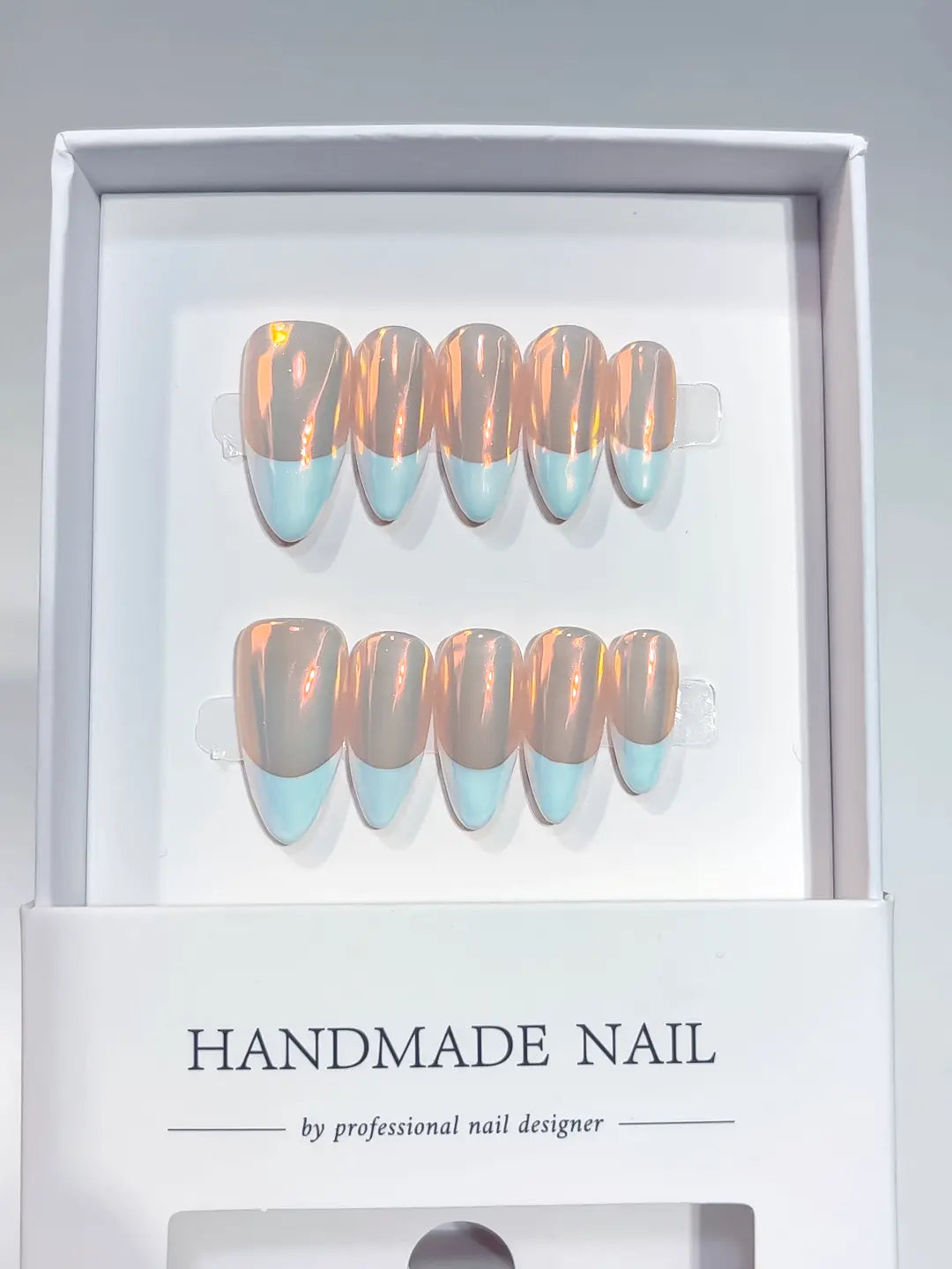 Close-up of aurora glazed medium almond handmade press on nails featuring light blue French tip design.

