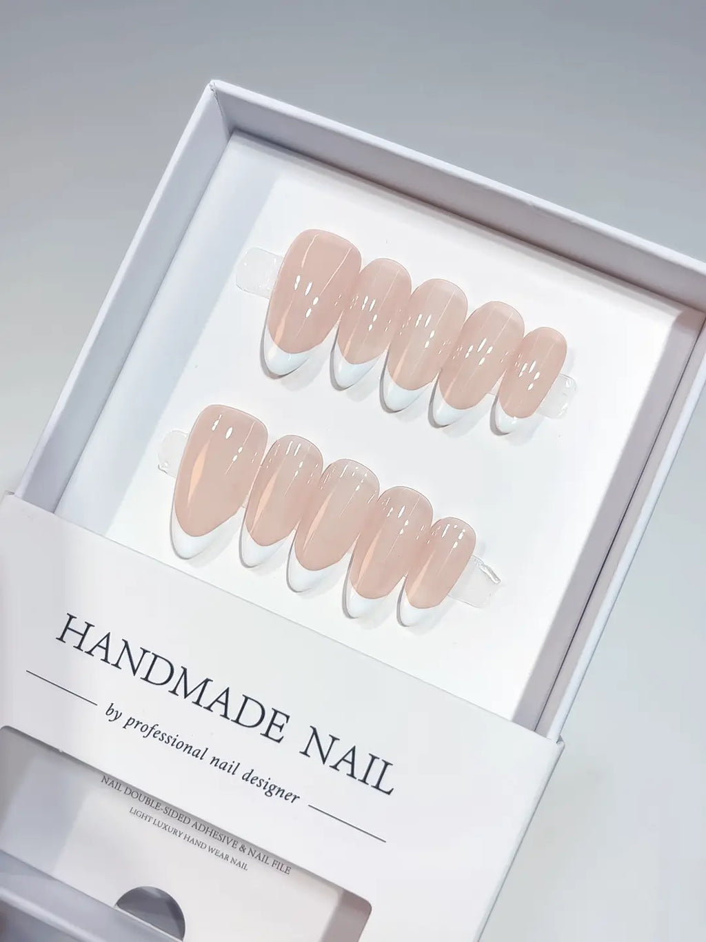 Elegant white french tips on pink nude medium almond handmade press on nails in luxury packaging.
