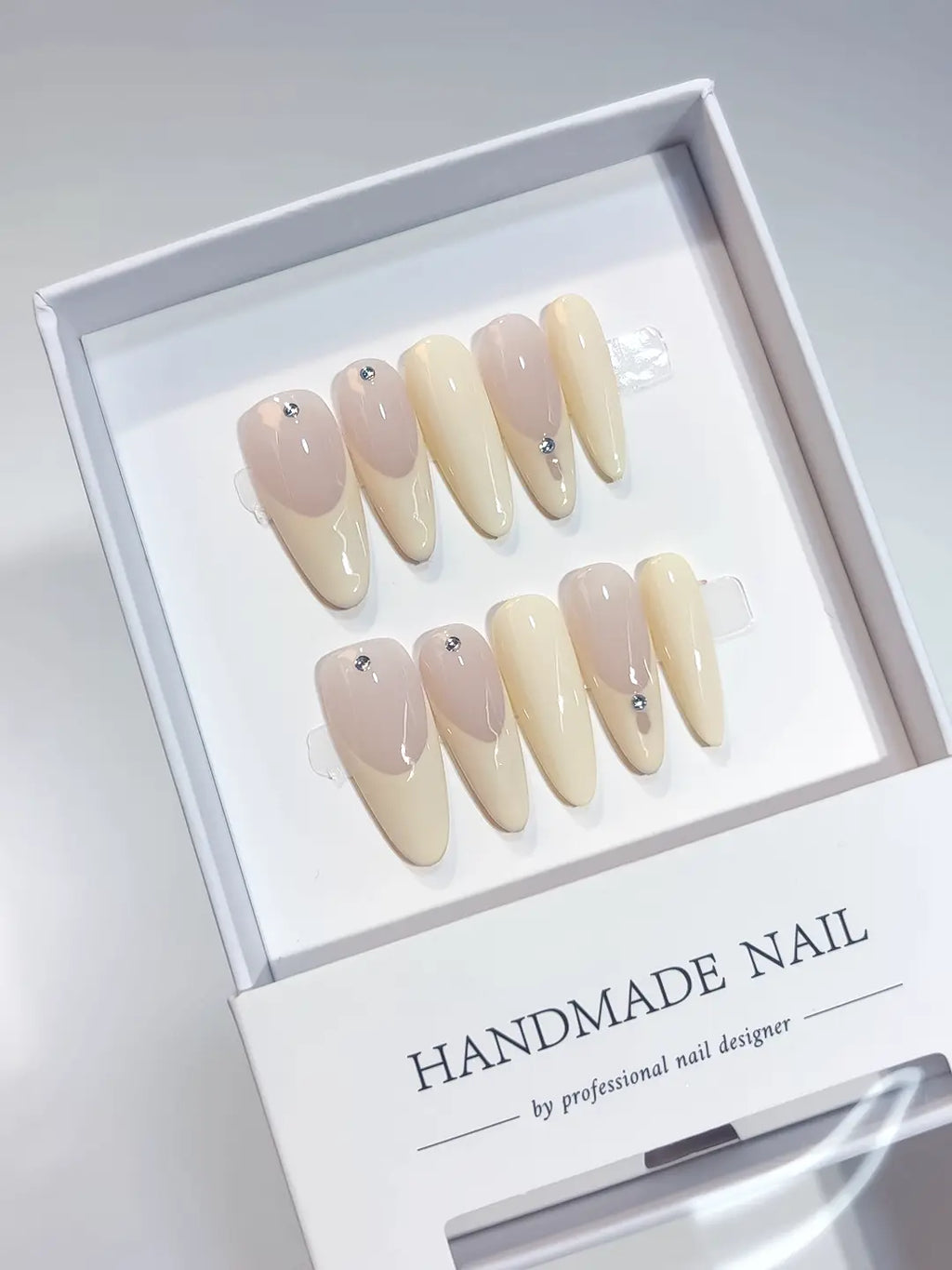 Full set of long oval handmade press on nails in a classic nude French style with jewelry accents.
