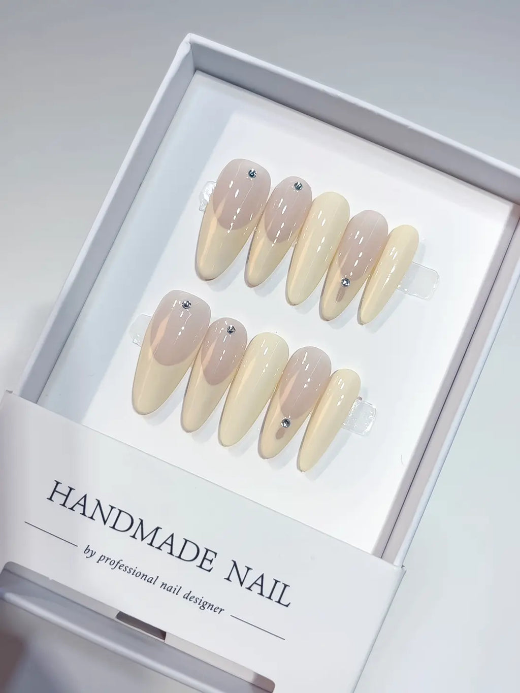 Long oval nude French handmade press on nails with tiny rhinestone details in a white box.
