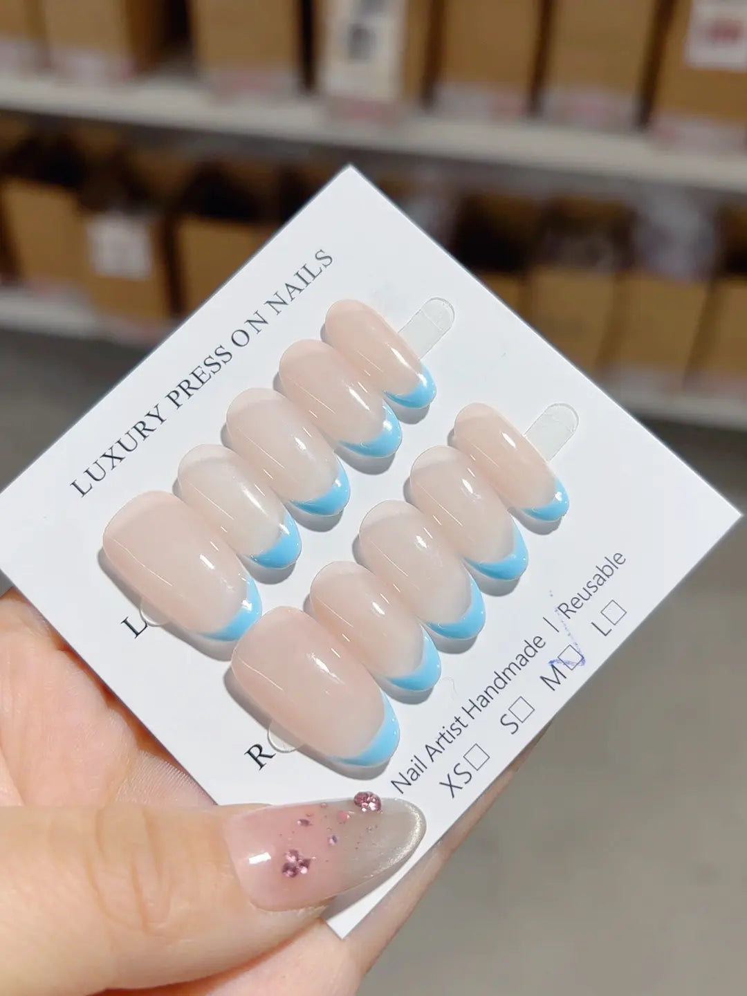 Nude oval handmade press on nails with blue French tips, angled view
