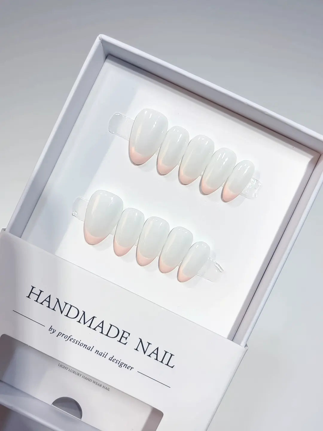 Short almond milky white handmade press on nails with soft pink French tips in a display box.
