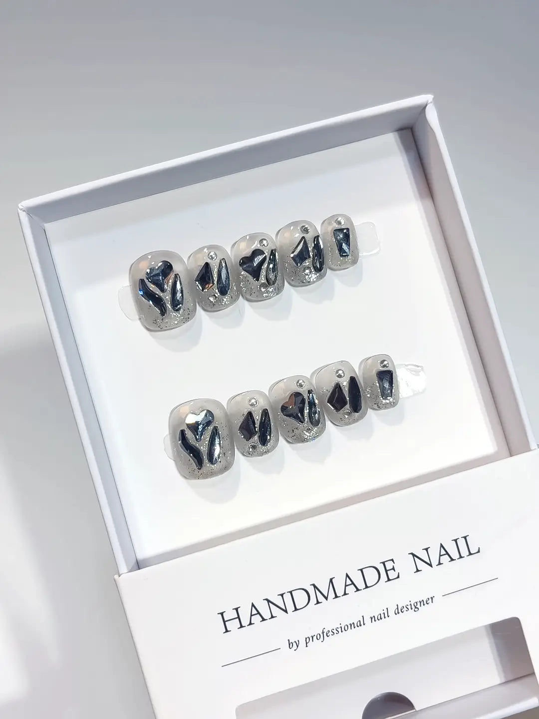 Short square silver glitter handmade press on nails with luxury 3D diamonds and black hearts in a white box.