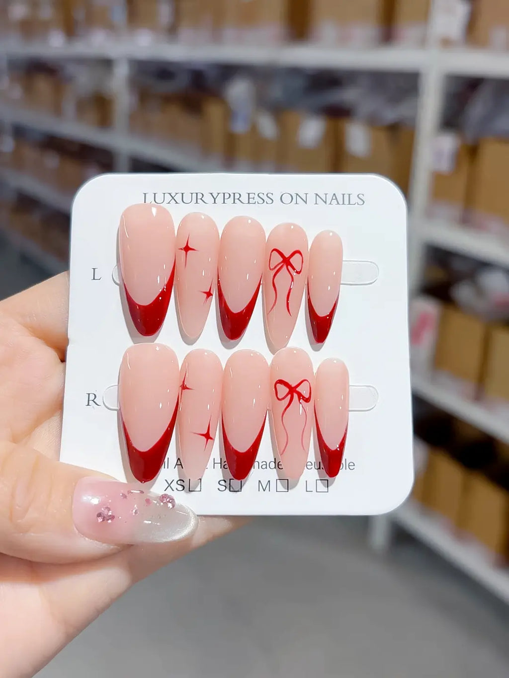 angled view showing deep red french tips on nude base, handmade press on nails with bow detail