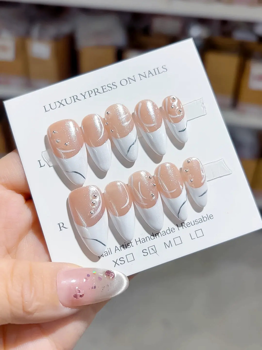 handmade press on nails, long stiletto nude & white french with swirl lines and rhinestones, angled view
