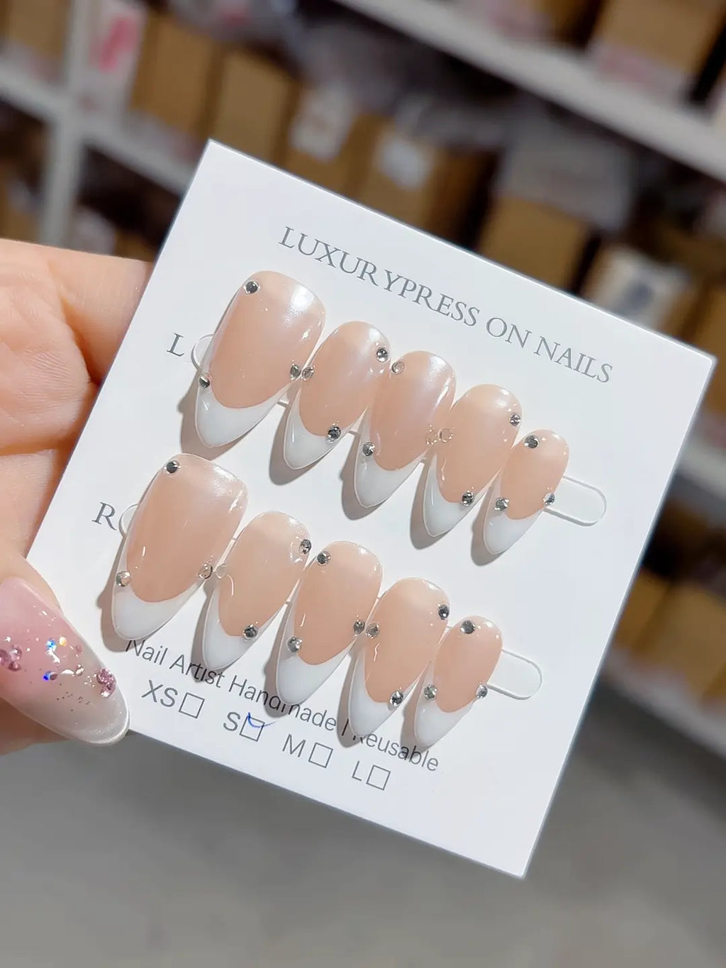 handmade press on nails, medium almond nude french with white tips and 3D rhinestones, angled view