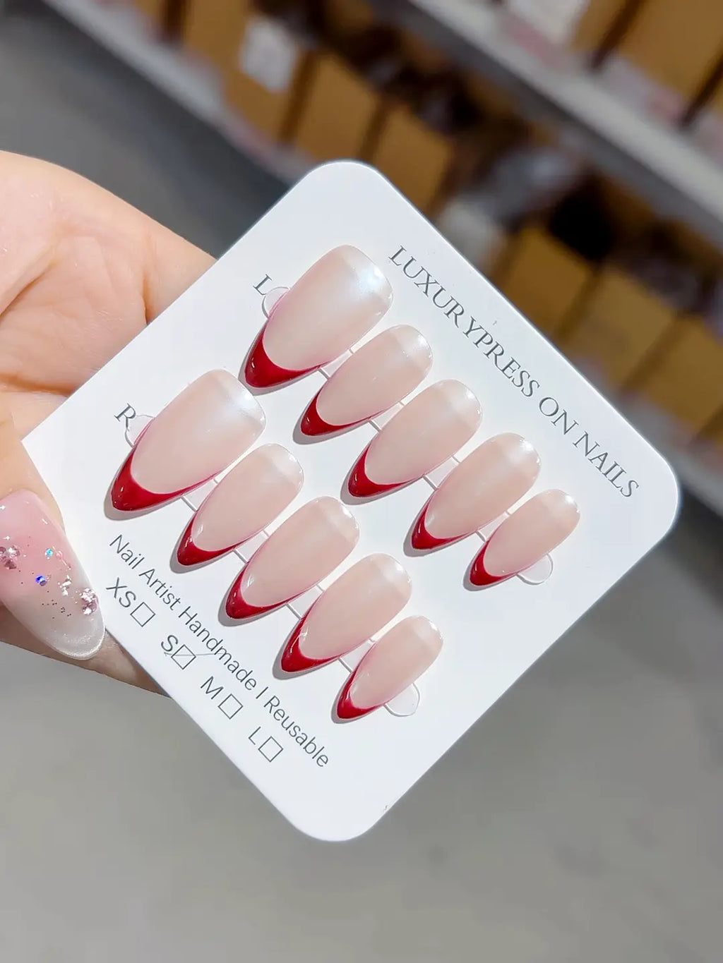 handmade press on nails, medium almond with nude base and bold red french tips, angled view