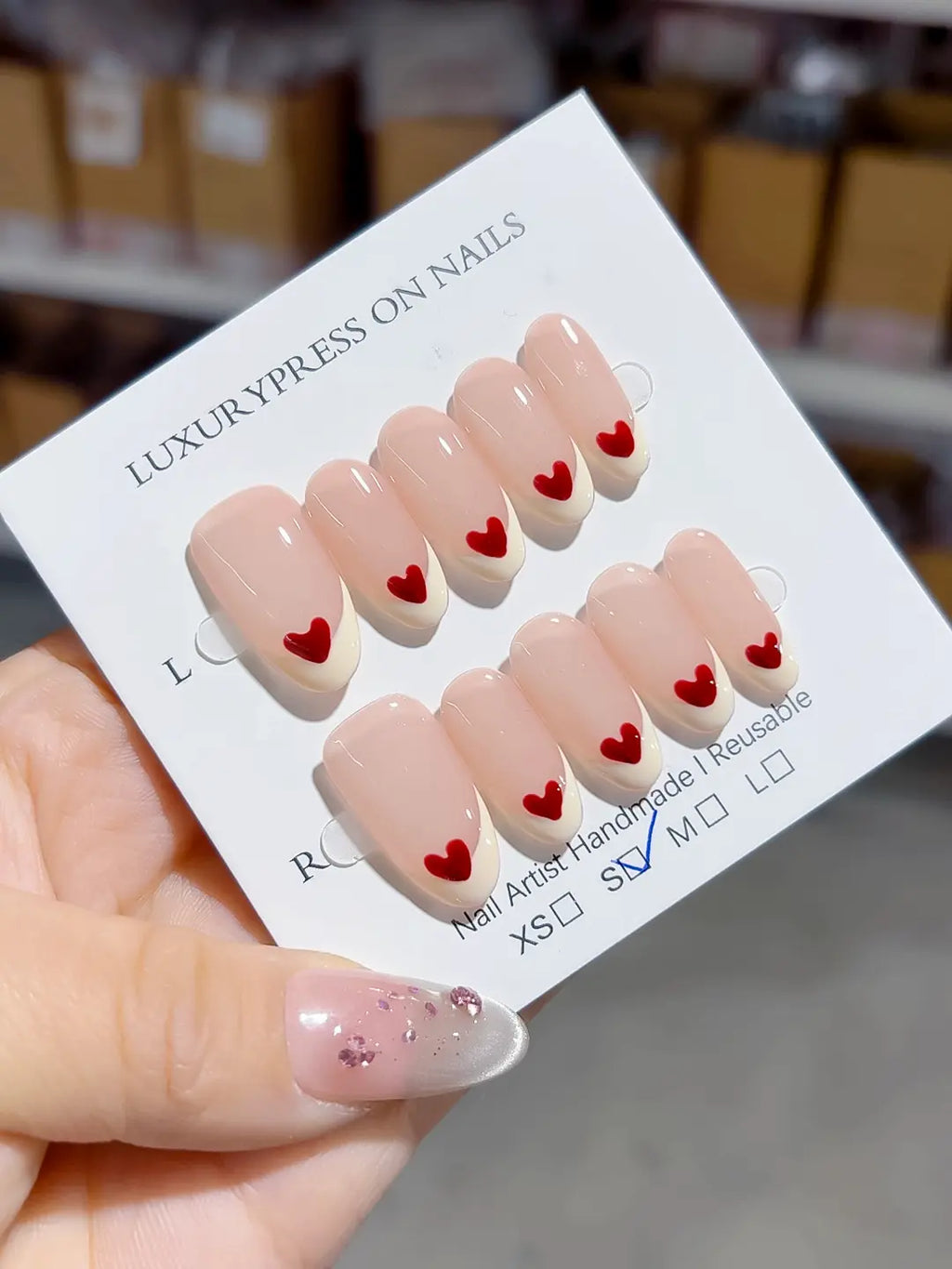 handmade press on nails, medium oval nude french with red heart accent on each tip, angled view