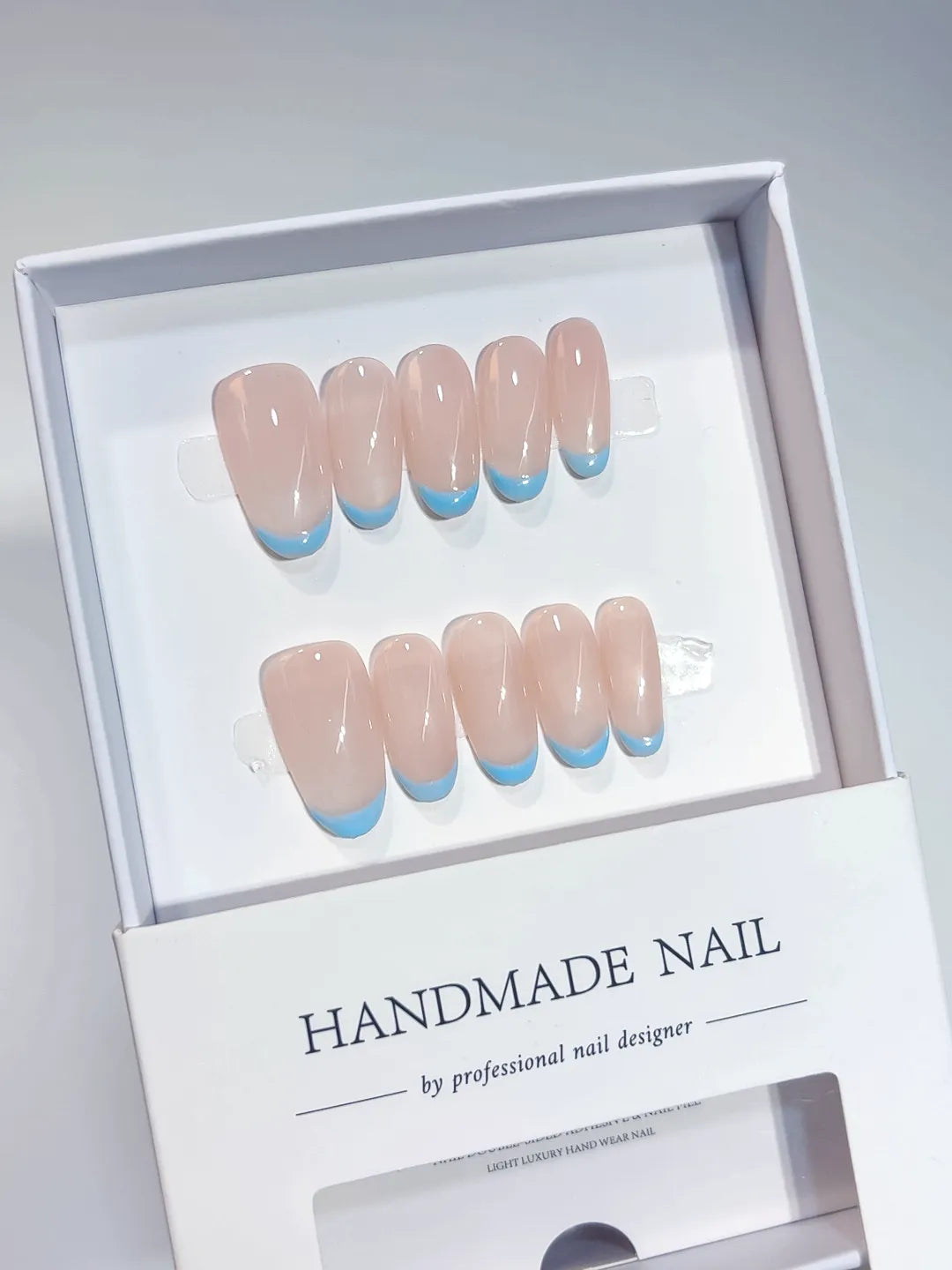 Nude oval handmade press on nails with blue French tips, angled view