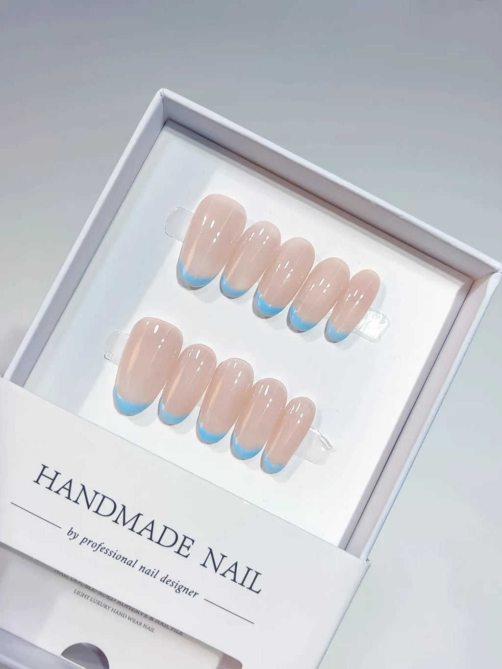 Nude oval handmade press on nails with blue French tips, angled view