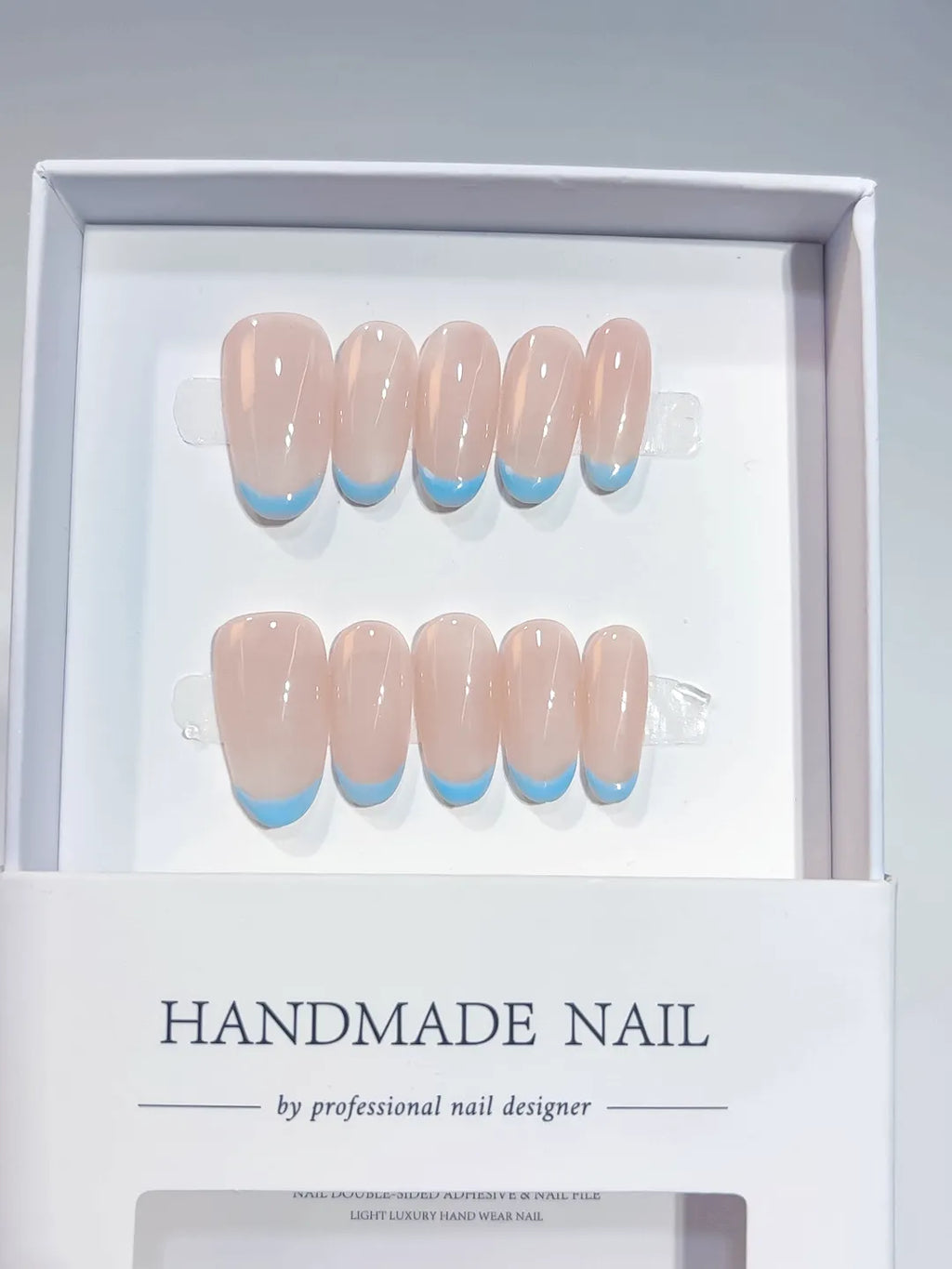 Nude oval handmade press on nails with blue French tips, angled view