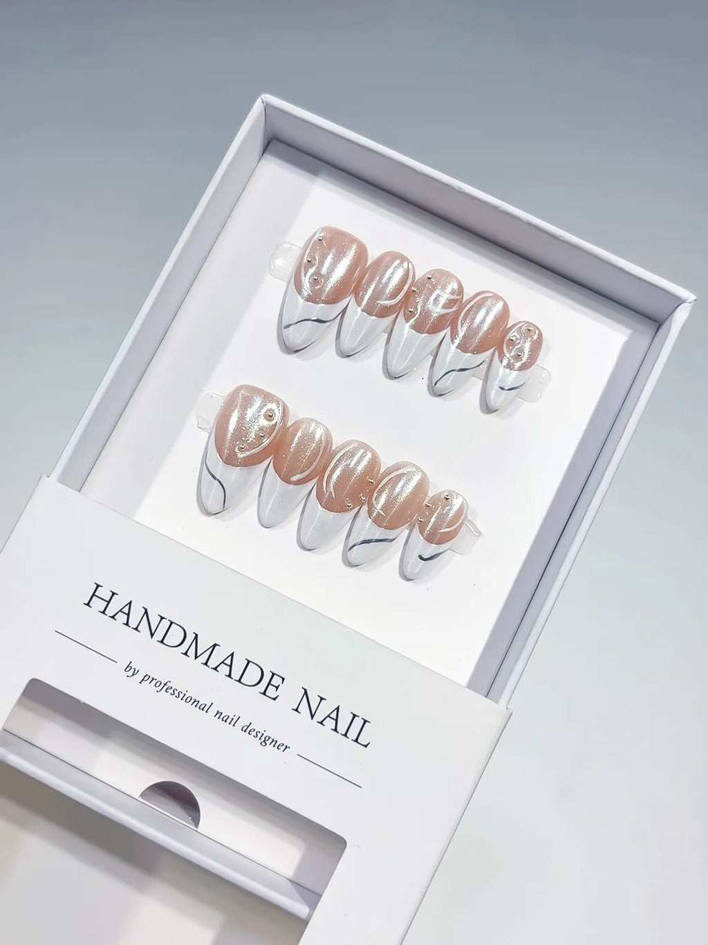 handmade press on nails, long stiletto nude & white french with swirl lines and rhinestones, angled view