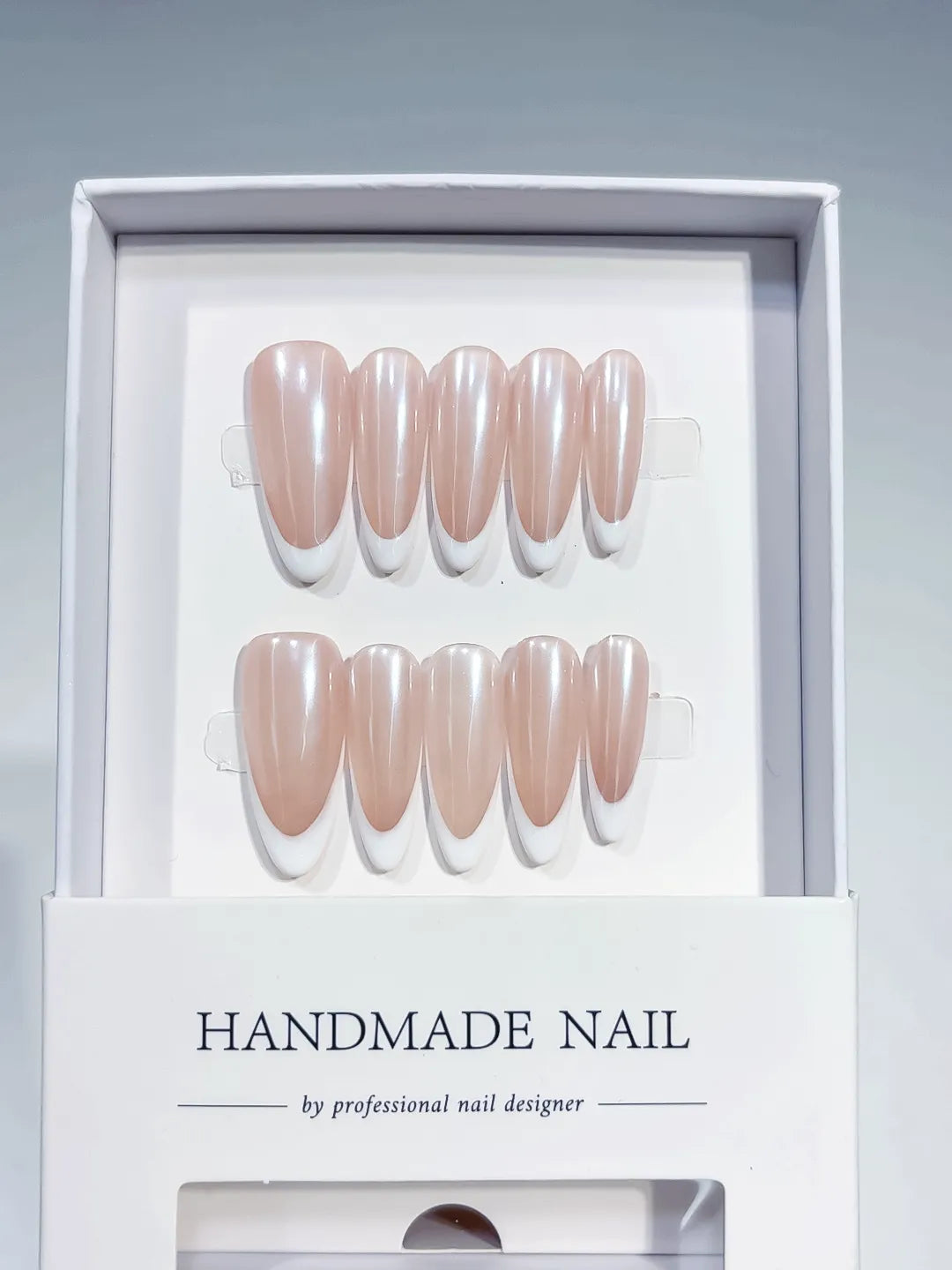 angled view of handmade press on nails, long almond nude French with white tips