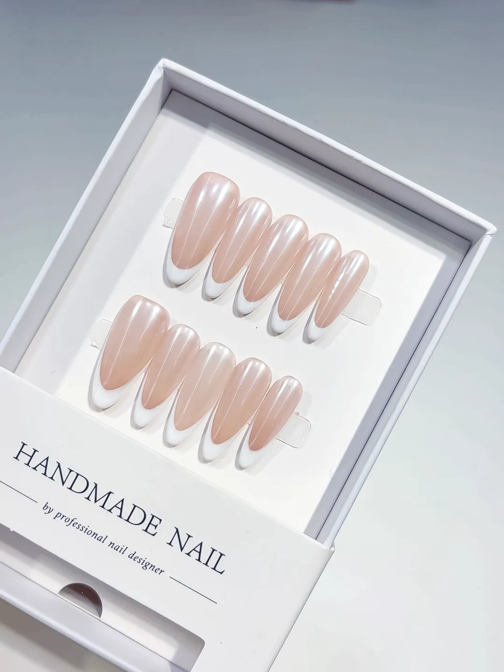 angled view of handmade press on nails, long almond nude French with white tips
