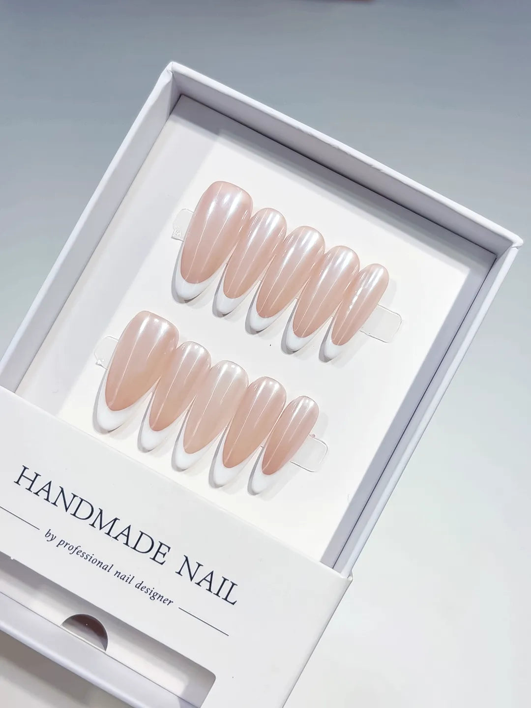 angled view of handmade press on nails, long almond nude French with white tips