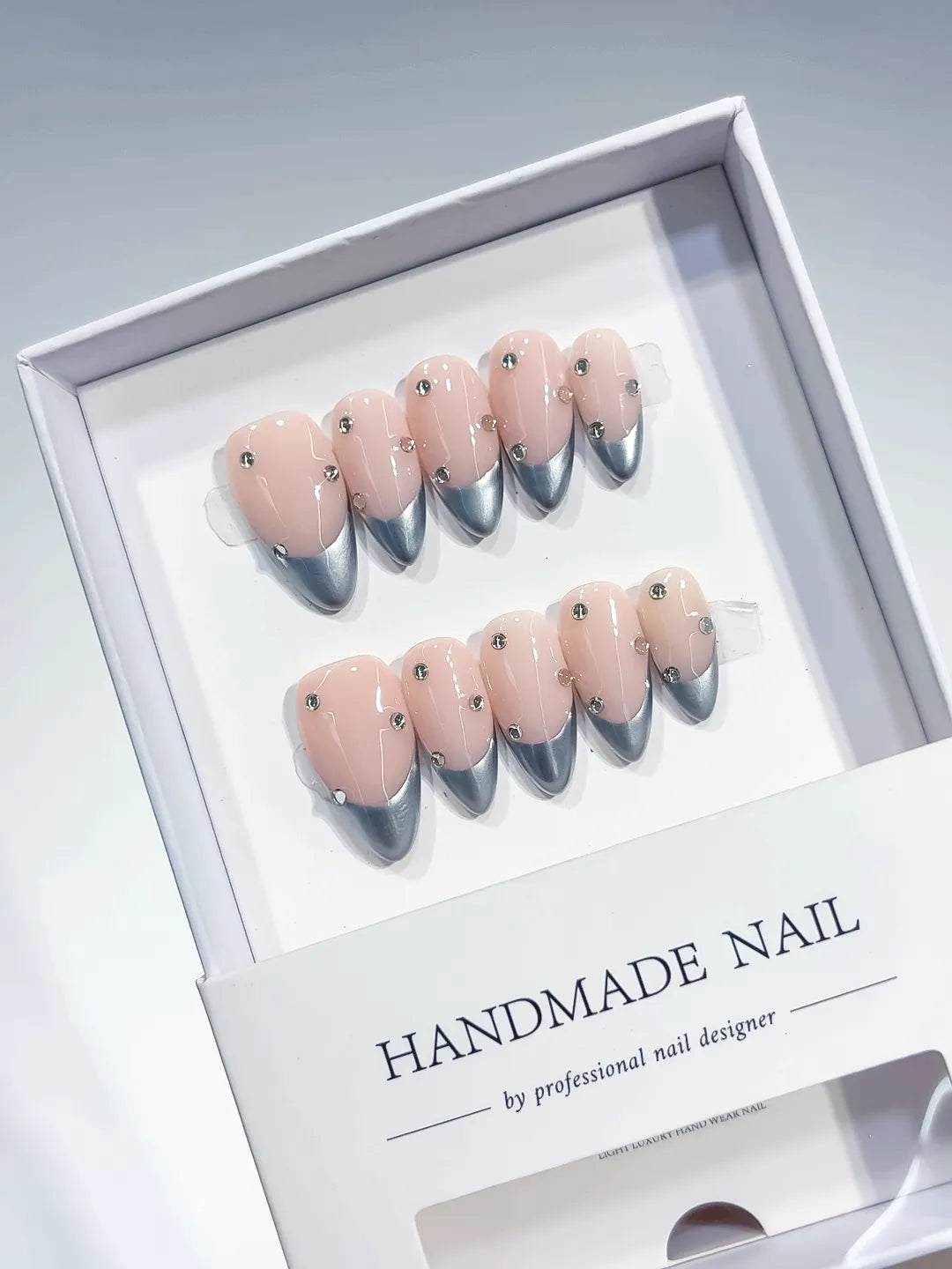 handmade press on nails, medium almond nude base with silver chrome french tips and 3D rhinestones, angled view