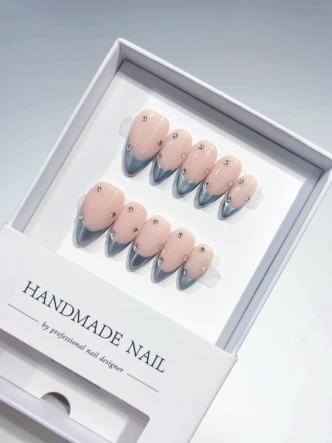 handmade press on nails, medium almond nude base with silver chrome french tips and 3D rhinestones, angled view