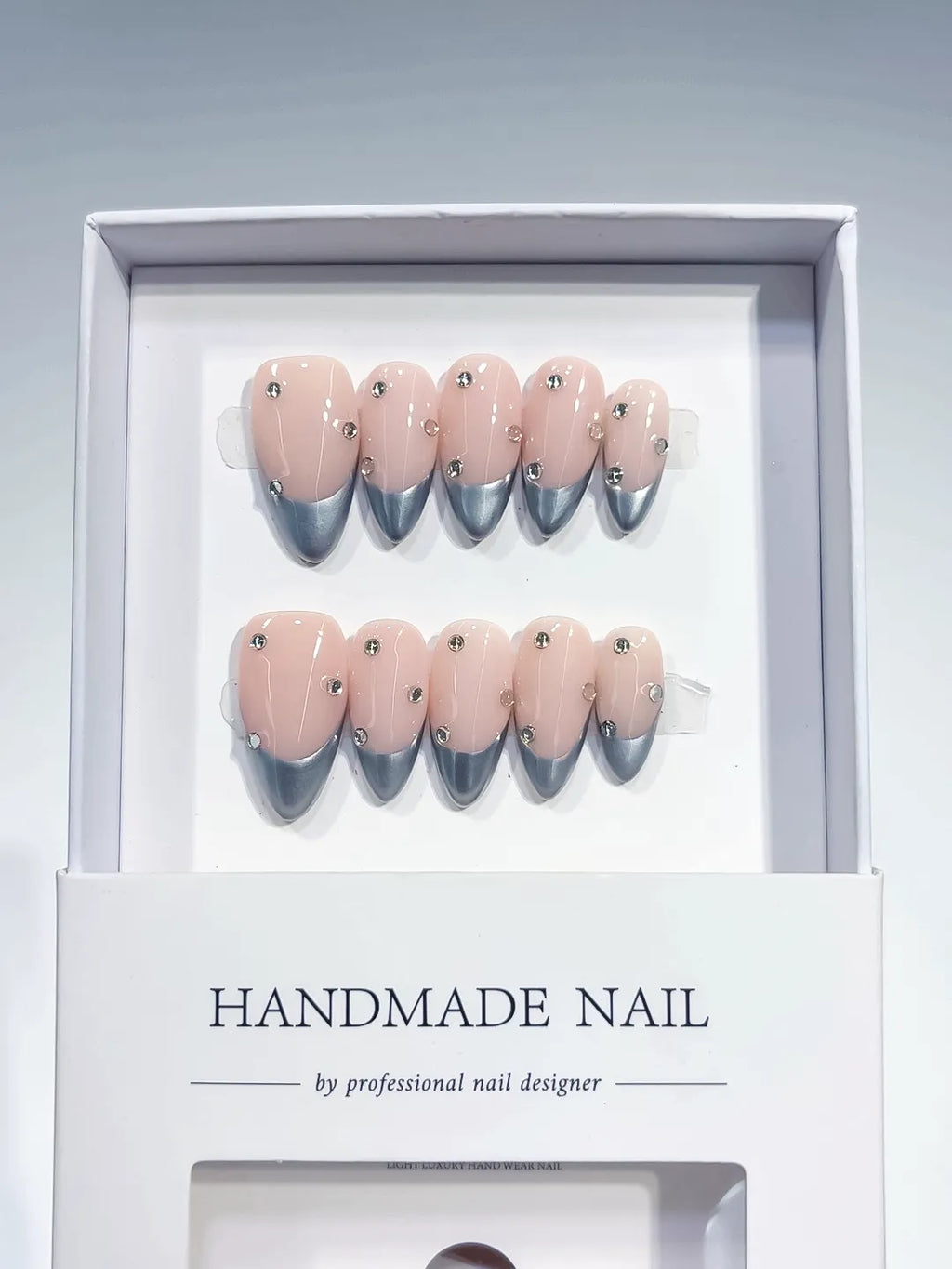 handmade press on nails, medium almond nude base with silver chrome french tips and 3D rhinestones, angled view