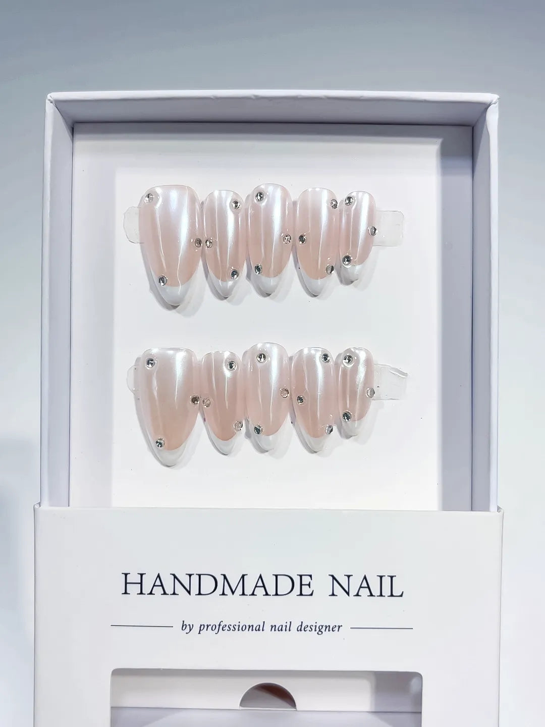 handmade press on nails, medium almond nude french with white tips and 3D rhinestones, angled view