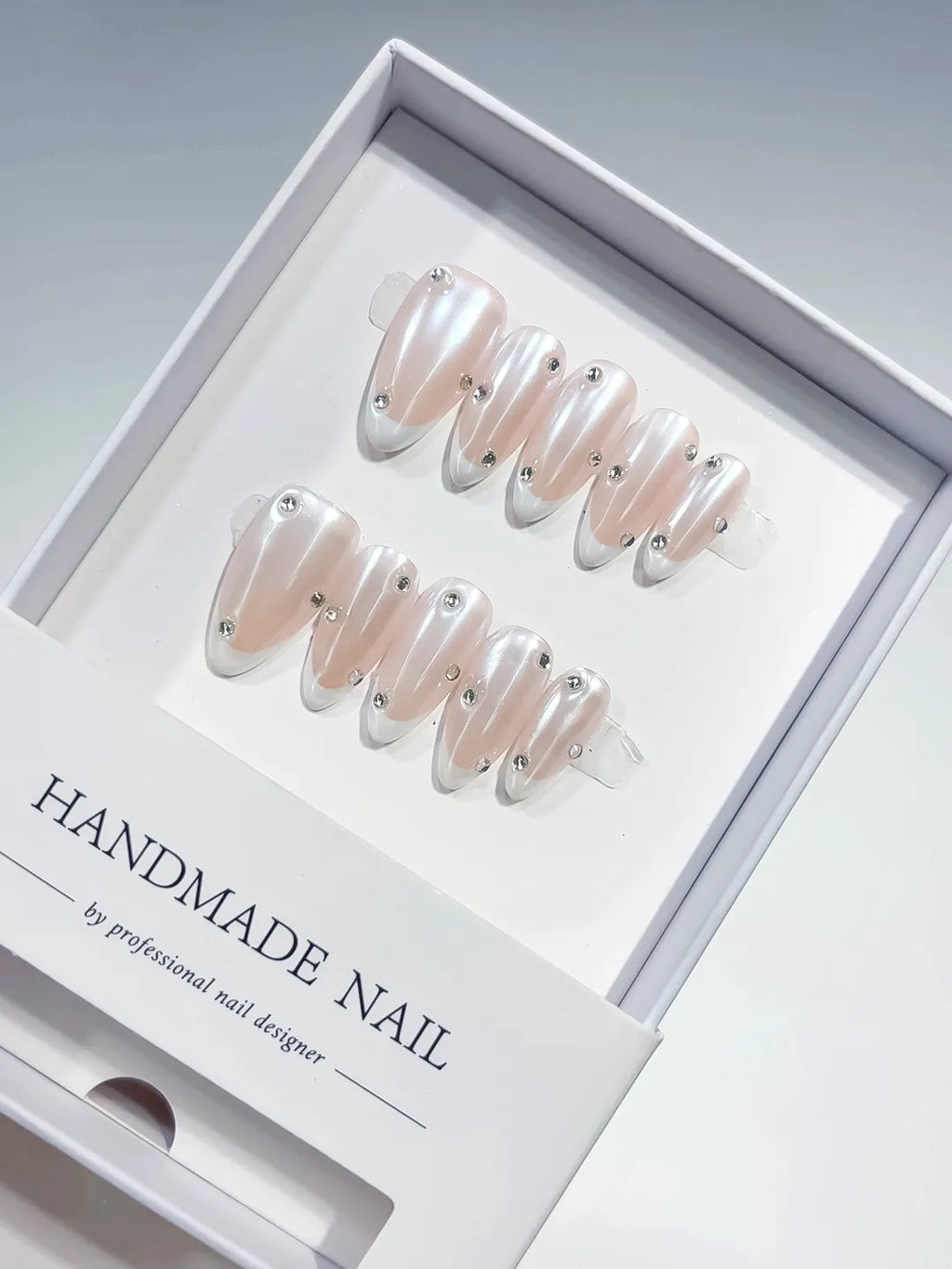 handmade press on nails, medium almond nude french with white tips and 3D rhinestones, angled view