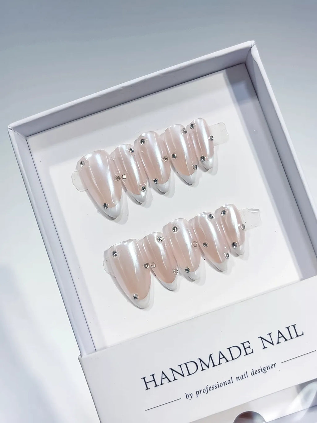 handmade press on nails, medium almond nude french with white tips and 3D rhinestones, angled view