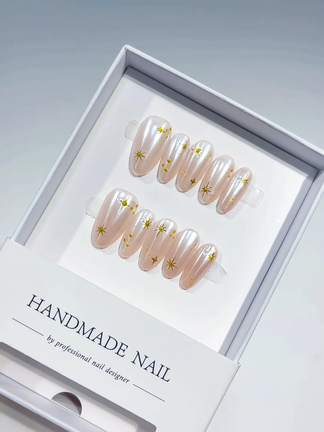 handmade press on nails, medium oval nude set with metallic gold print accents, angled view
