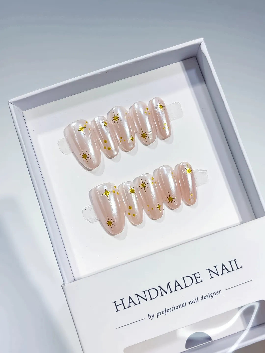 handmade press on nails, medium oval nude set with metallic gold print accents, angled view