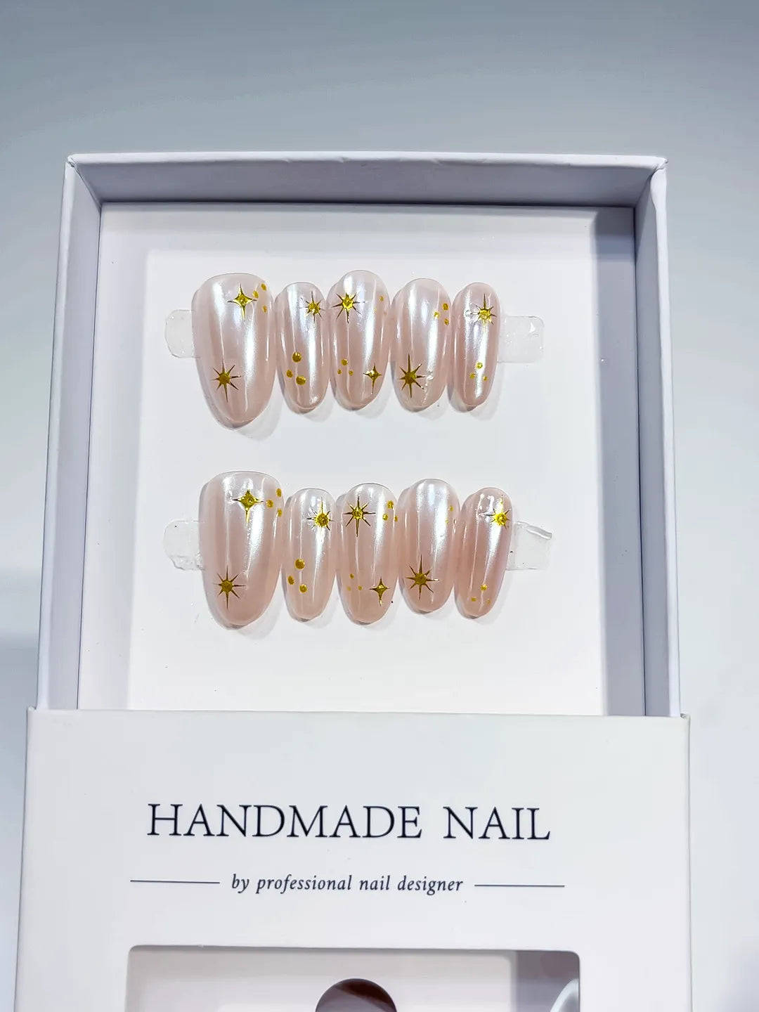 handmade press on nails, medium oval nude set with metallic gold print accents, angled view
